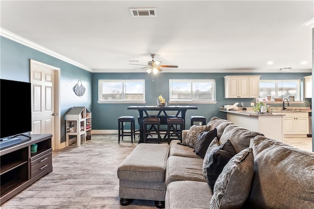 living area featuring light wood finished floors, visible vents, ceiling fan, baseboards, and ornamental molding