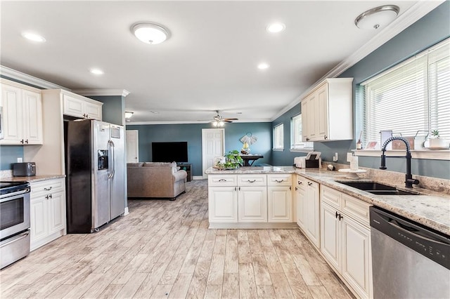 kitchen featuring a peninsula, a sink, stainless steel appliances, open floor plan, and light wood-type flooring