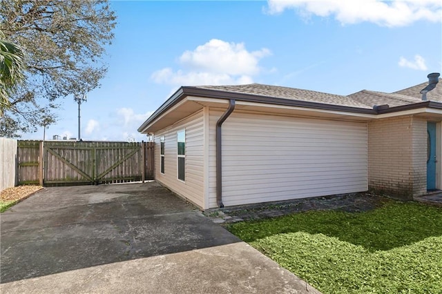 view of side of property with a gate, brick siding, a shingled roof, and fence