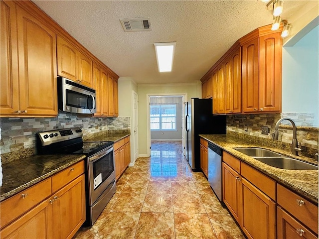 kitchen featuring visible vents, dark stone countertops, brown cabinetry, stainless steel appliances, and a sink