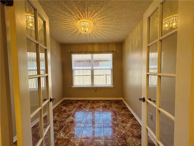 tiled empty room with french doors, baseboards, and a textured ceiling