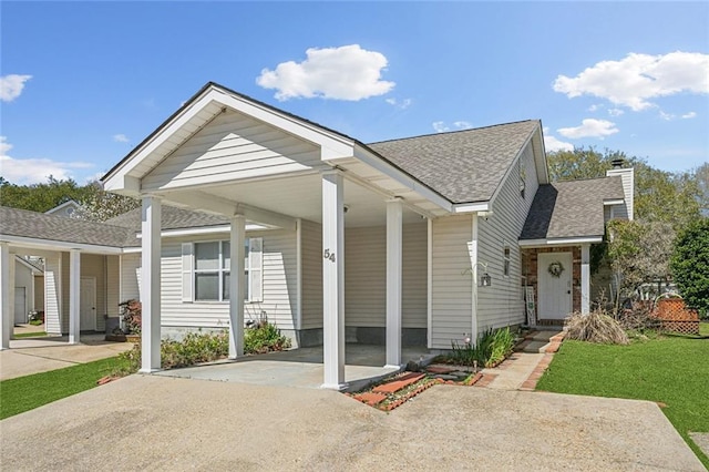 view of front of home featuring a front lawn, roof with shingles, a chimney, a carport, and driveway