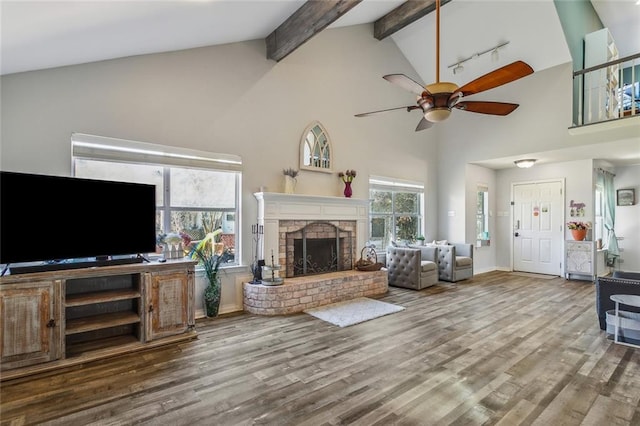 living area with wood finished floors, a ceiling fan, high vaulted ceiling, a fireplace, and beamed ceiling