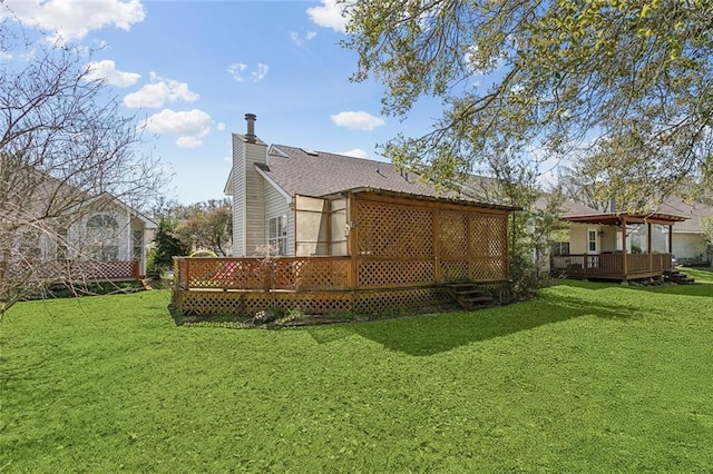 back of house featuring a deck, a lawn, roof with shingles, and a chimney