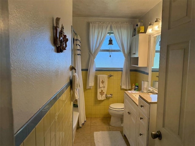 full bathroom featuring vanity, wainscoting, tile patterned floors, toilet, and tile walls