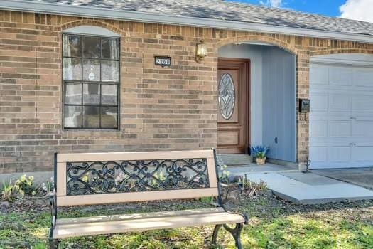 doorway to property featuring brick siding, a garage, and roof with shingles