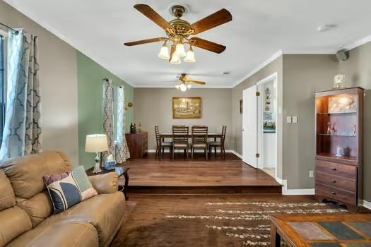 living area featuring ornamental molding, a ceiling fan, baseboards, and wood finished floors