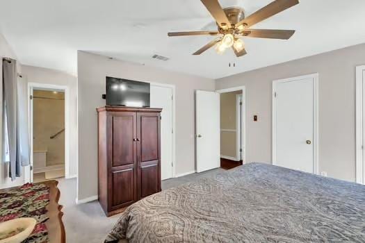 carpeted bedroom featuring ensuite bath, visible vents, two closets, and ceiling fan