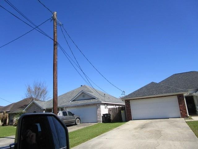 view of home's exterior featuring driveway, fence, roof with shingles, an attached garage, and brick siding