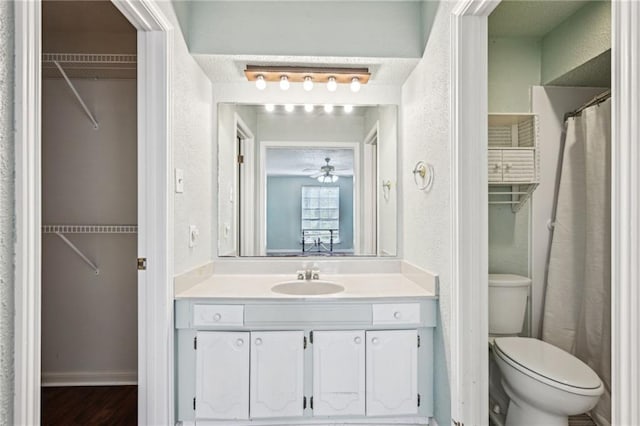 bathroom with a spacious closet, toilet, vanity, and a textured wall