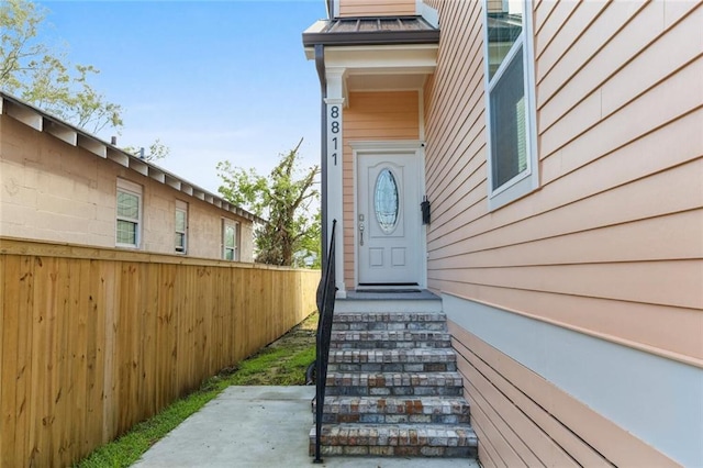 view of exterior entry featuring a standing seam roof, fence, and metal roof