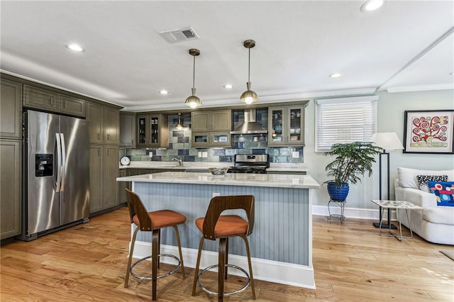 kitchen featuring visible vents, a sink, glass insert cabinets, appliances with stainless steel finishes, and wall chimney exhaust hood