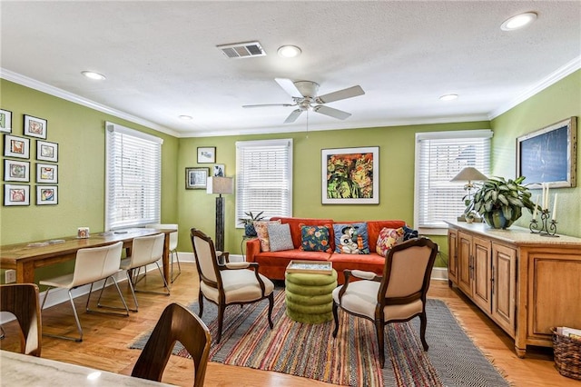 living room with baseboards, visible vents, light wood finished floors, ceiling fan, and ornamental molding