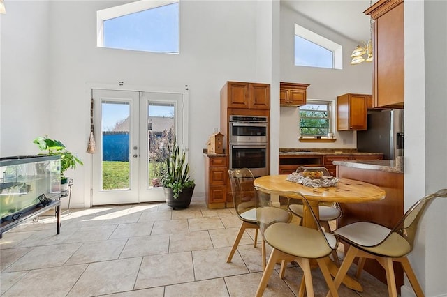 kitchen with light tile patterned floors, brown cabinetry, a high ceiling, french doors, and appliances with stainless steel finishes