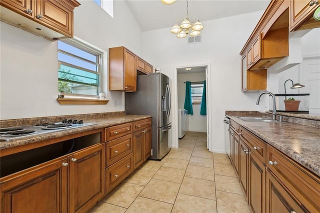 kitchen featuring dark countertops, light tile patterned floors, brown cabinets, stainless steel appliances, and a sink