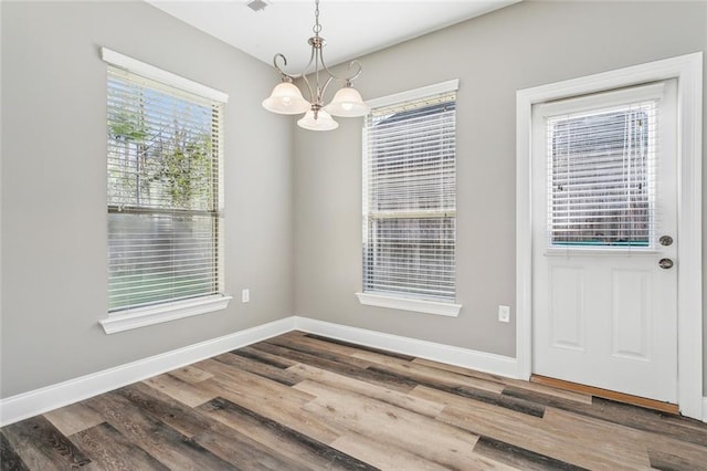 unfurnished dining area with baseboards, an inviting chandelier, and wood finished floors