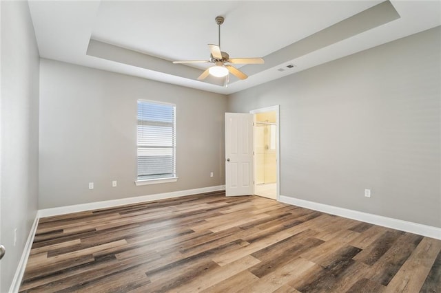 spare room featuring baseboards, a ceiling fan, a tray ceiling, and wood finished floors