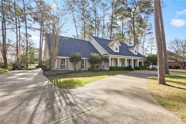 new england style home with concrete driveway, a front yard, and roof with shingles