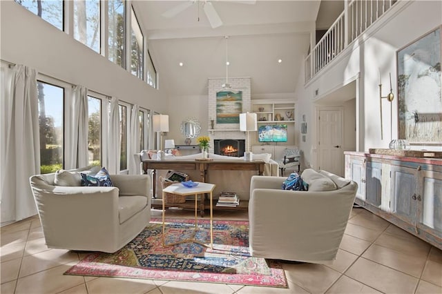 living room with a ceiling fan, high vaulted ceiling, beam ceiling, light tile patterned flooring, and a warm lit fireplace