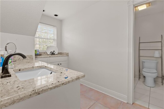 bathroom featuring vanity, baseboards, vaulted ceiling, tile patterned floors, and toilet