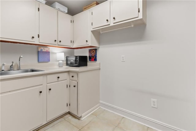 kitchen with black microwave, light countertops, light tile patterned floors, white cabinets, and a sink