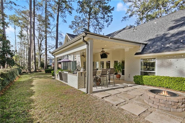 rear view of property with a patio, a yard, ceiling fan, a shingled roof, and brick siding