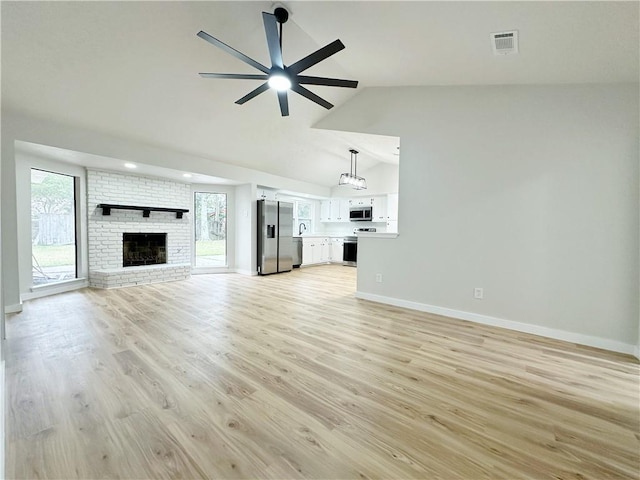 unfurnished living room with plenty of natural light, a brick fireplace, light wood-type flooring, and a ceiling fan