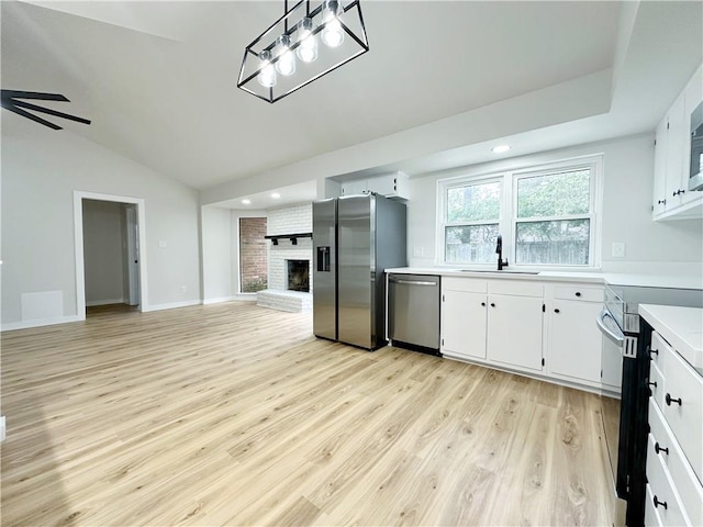 kitchen featuring a sink, stainless steel appliances, light countertops, a brick fireplace, and open floor plan