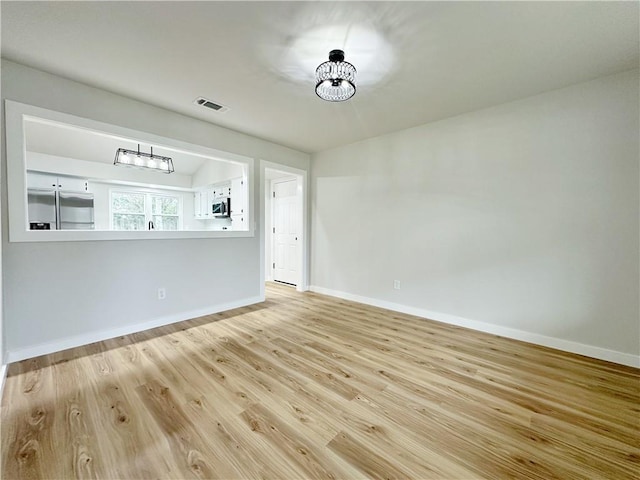 unfurnished living room featuring a notable chandelier, wood finished floors, visible vents, and baseboards