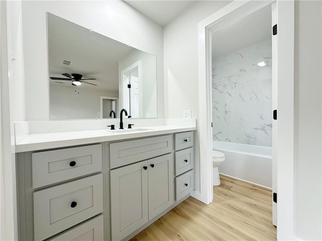 bathroom featuring vanity, wood finished floors, a ceiling fan, shower / bathing tub combination, and toilet