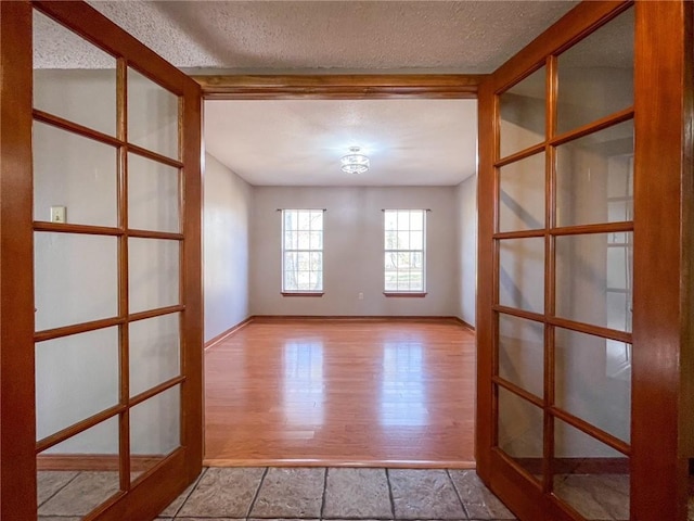 unfurnished room with beamed ceiling, light wood-style flooring, a textured ceiling, french doors, and baseboards