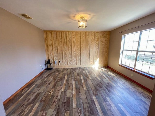 unfurnished room with wood finished floors, visible vents, wood walls, and baseboards