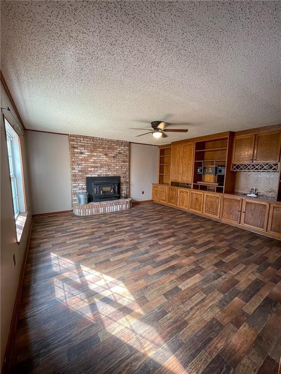 unfurnished living room with baseboards, a textured ceiling, a ceiling fan, and dark wood-style flooring