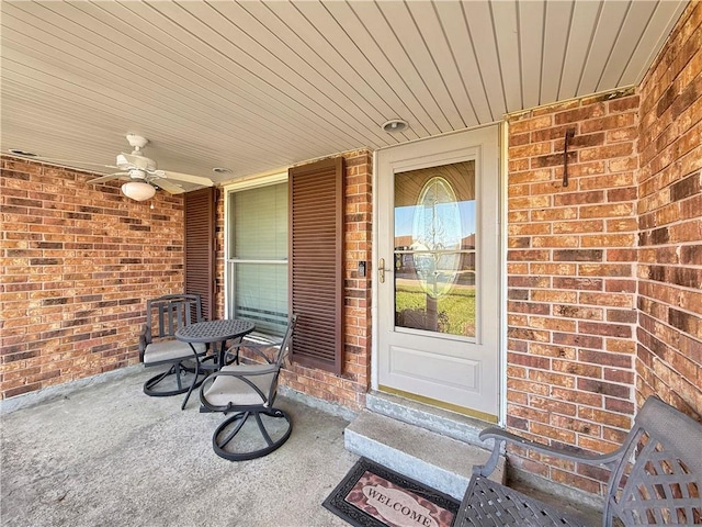 view of exterior entry featuring a porch, brick siding, and ceiling fan