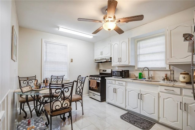 kitchen with stainless steel range with gas stovetop, a sink, light countertops, white cabinets, and under cabinet range hood