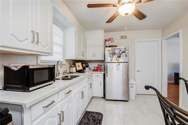 kitchen with a sink, freestanding refrigerator, white cabinets, black microwave, and ceiling fan