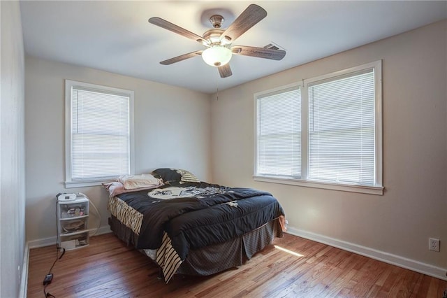 bedroom featuring baseboards, multiple windows, wood finished floors, and a ceiling fan