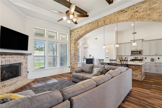 living room with ornamental molding, dark wood-style floors, arched walkways, a high ceiling, and a fireplace