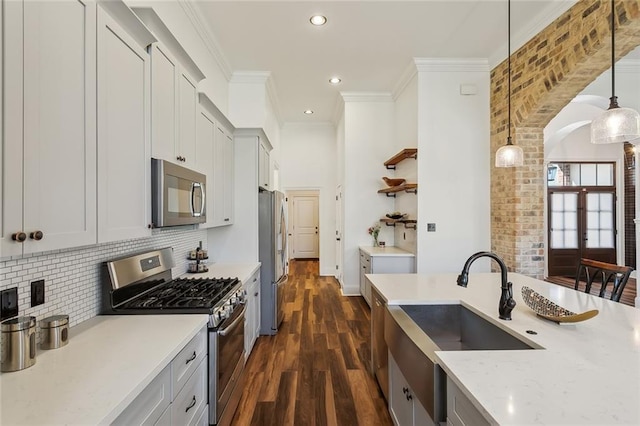 kitchen featuring a sink, stainless steel appliances, arched walkways, crown molding, and hanging light fixtures