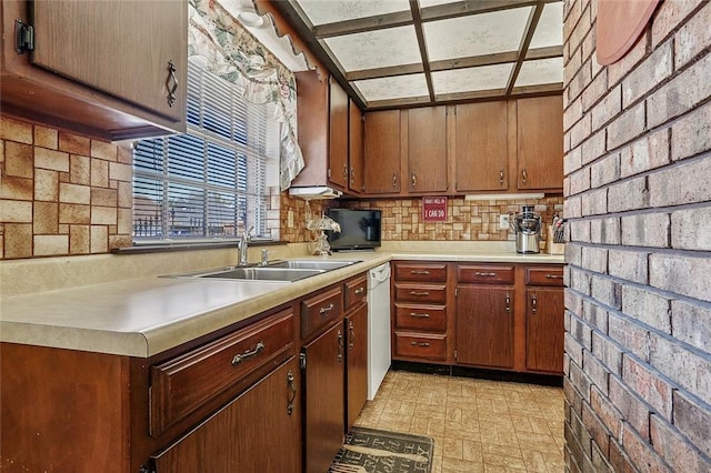 kitchen featuring brick wall, white dishwasher, a sink, decorative backsplash, and light countertops