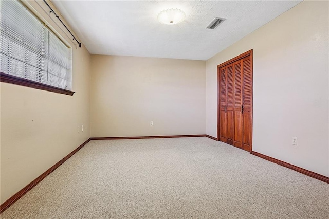 carpeted spare room featuring visible vents, a textured ceiling, and baseboards