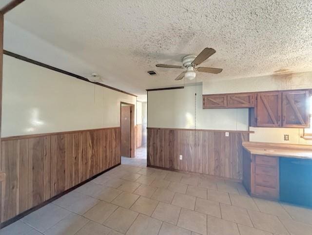 kitchen with wooden walls, visible vents, ceiling fan, wainscoting, and a textured ceiling