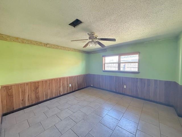 empty room with a textured ceiling, wooden walls, and wainscoting