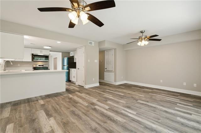 unfurnished living room featuring a sink, visible vents, baseboards, and wood finished floors