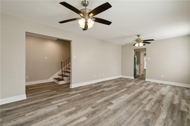 empty room featuring stairs, wood finished floors, baseboards, and ceiling fan