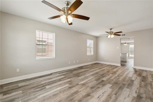 empty room featuring ceiling fan, visible vents, baseboards, and wood finished floors