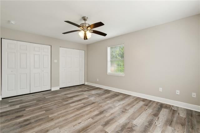 unfurnished bedroom featuring baseboards, multiple closets, wood finished floors, and a ceiling fan