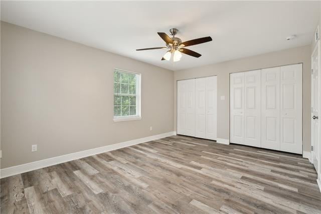 unfurnished bedroom featuring ceiling fan, two closets, baseboards, and wood finished floors