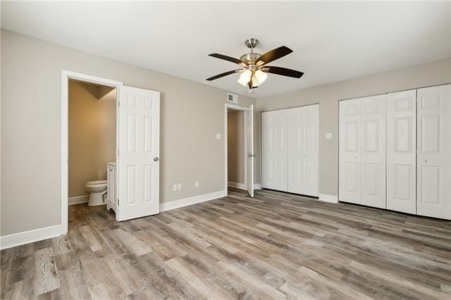 unfurnished bedroom featuring visible vents, baseboards, two closets, and wood finished floors