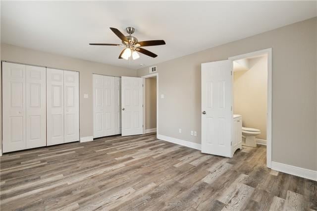 unfurnished bedroom featuring wood finished floors, baseboards, and multiple closets